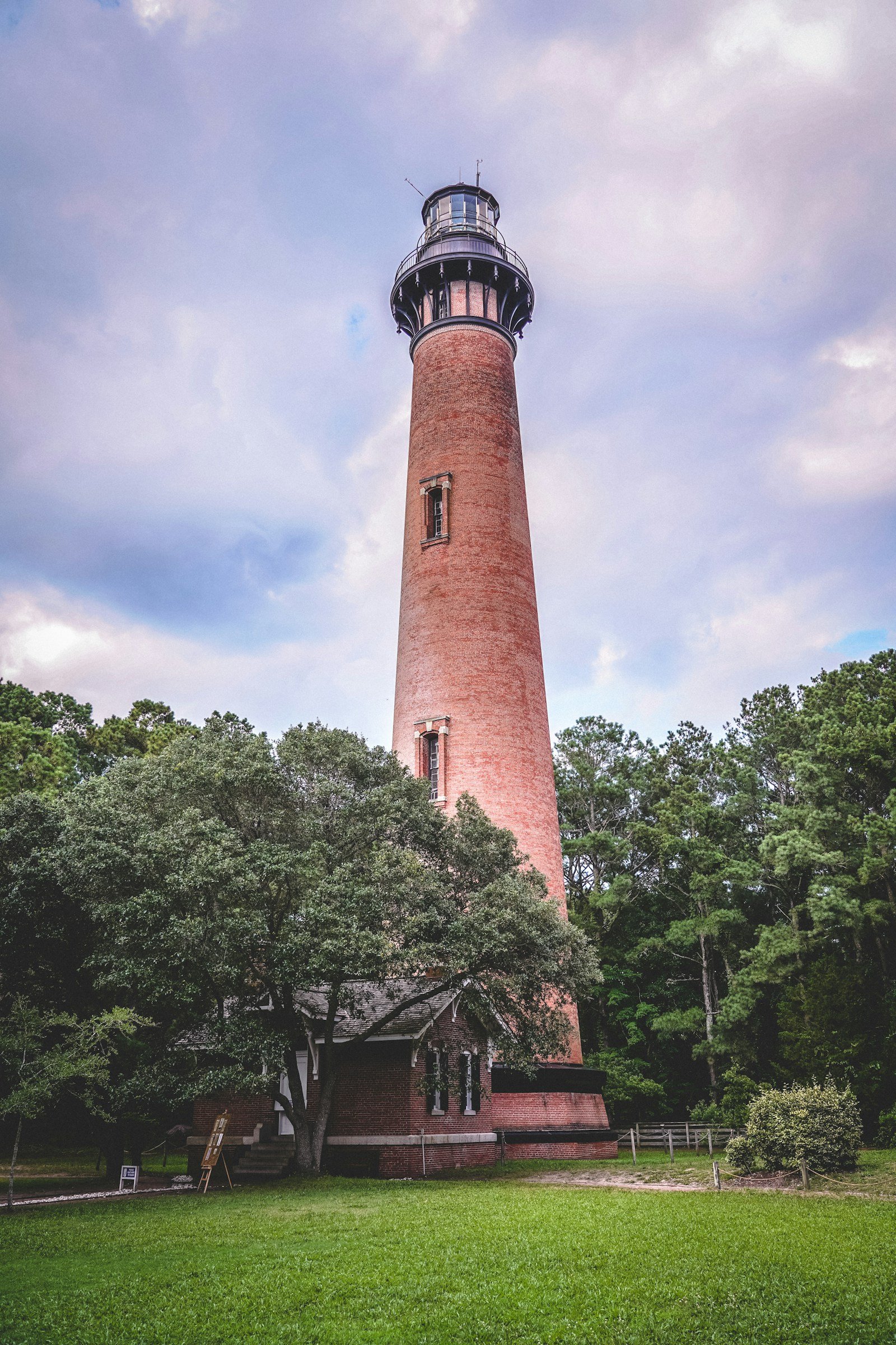 Currituck Beach Lighthouse red brick tower rising above green trees, Corolla NC