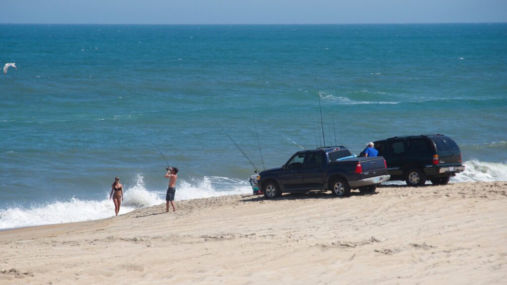 Vehicles and visitors spread along the water's edge on a wide beach at Cape Hatteras National Seashore.