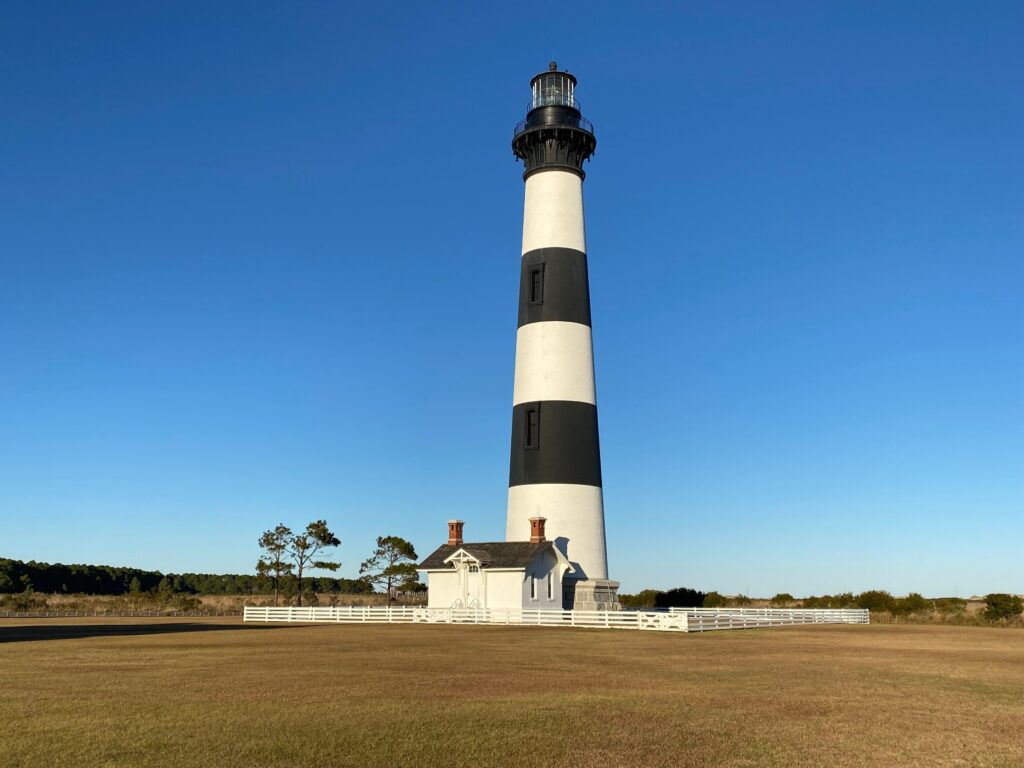 The black-and-white horizontally banded tower of the Bodie Island Lighthouse rising above the trees.