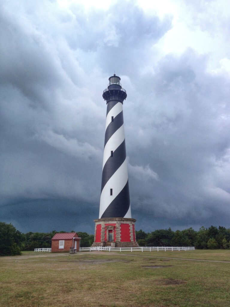 The striped Cape Hatteras Lighthouse tower against a dark, heavy sky.