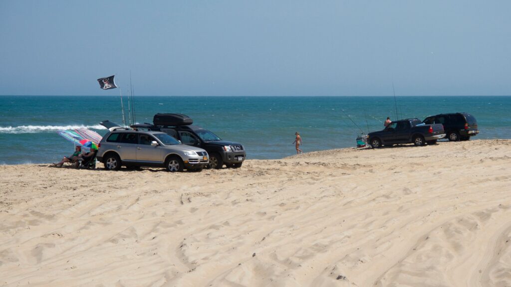 Several four-wheel-drive vehicles parked above the surf line on a wide sand beach.