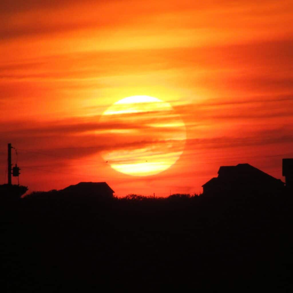 A deep red sun dropping toward the horizon over dark water at Frisco.