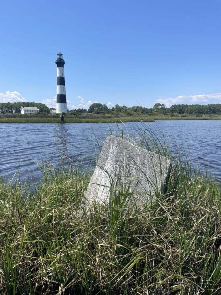 A weathered granite marker standing in grass beside the sound, one of four that delineate an old light station reservation.