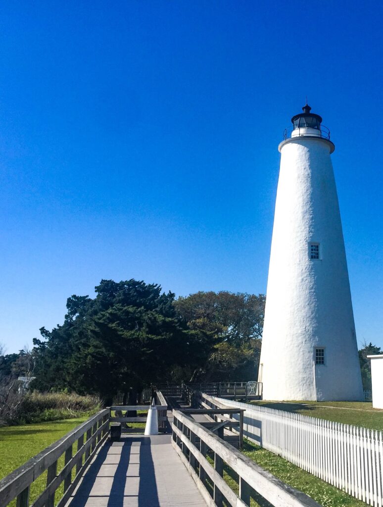 The short white tower of the Ocracoke Lighthouse against a clear blue sky.
