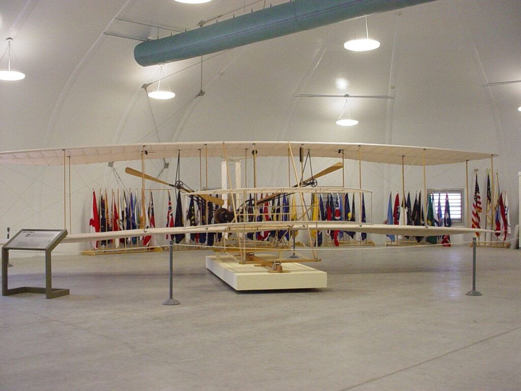 A full-size reproduction of the 1903 Wright Flyer on display inside a hangar-style building.