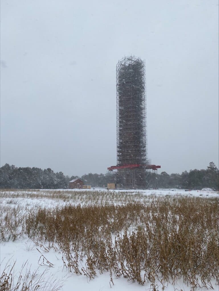 The Cape Hatteras Lighthouse tower rising through falling snow and low cloud.