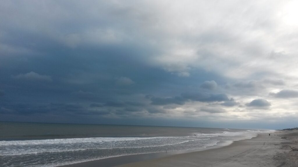 A heavy bank of dark storm cloud building over a wide, empty beach.