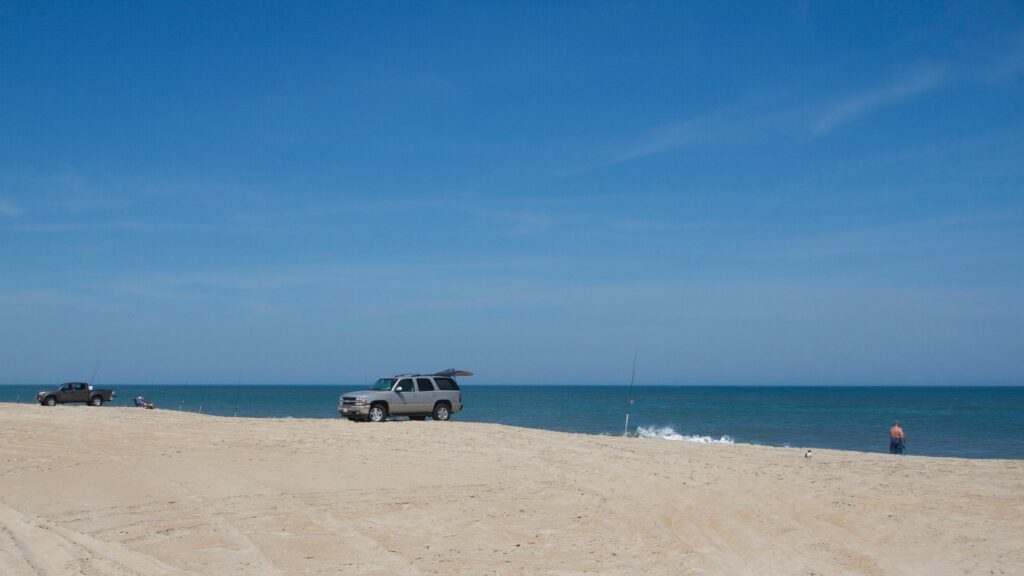 Four-wheel-drive vehicles parked in a line on the sand along an ORV beach route.